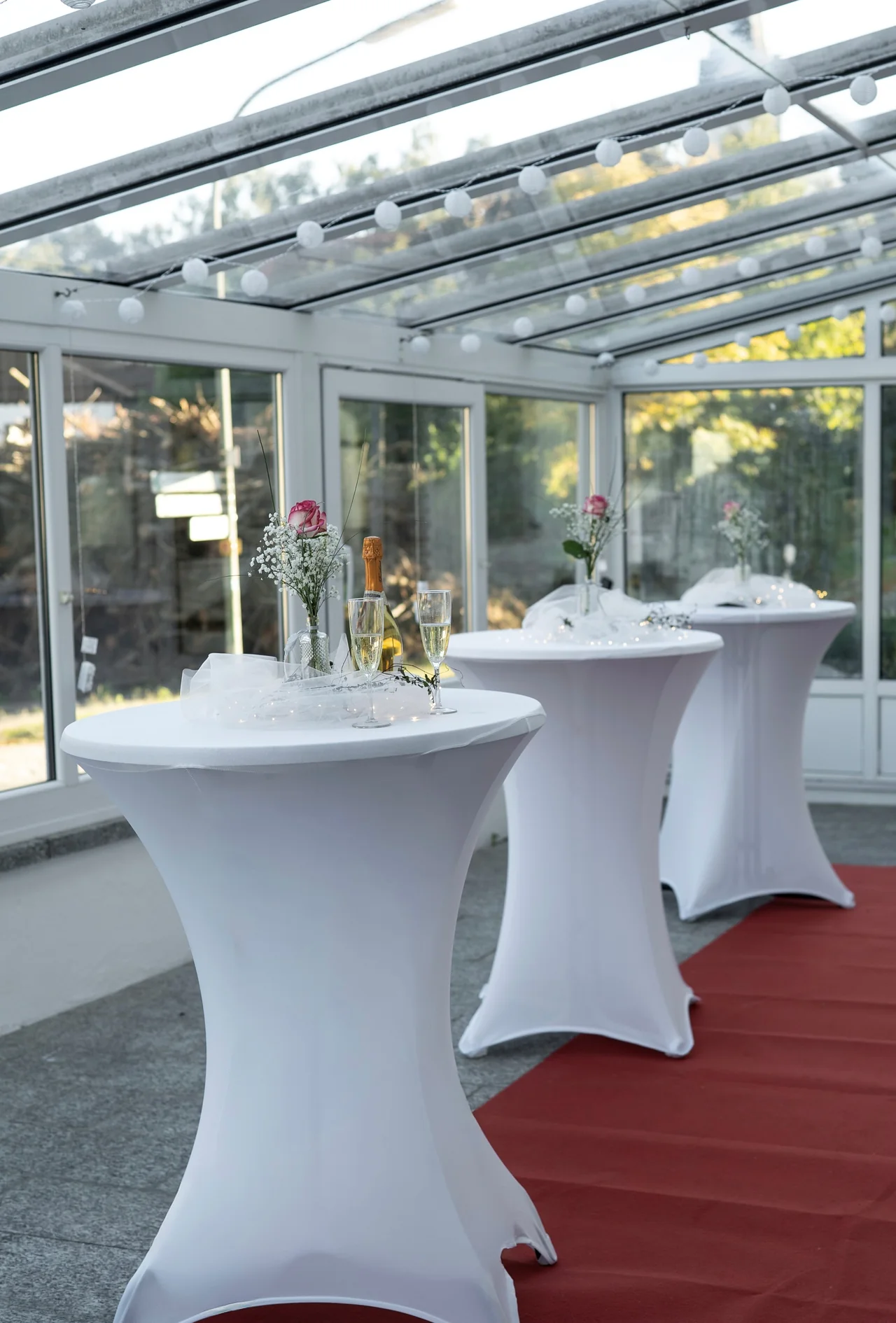 Heller Wintergarten mit festlich dekorierten Stehtischen für den Sektempfang